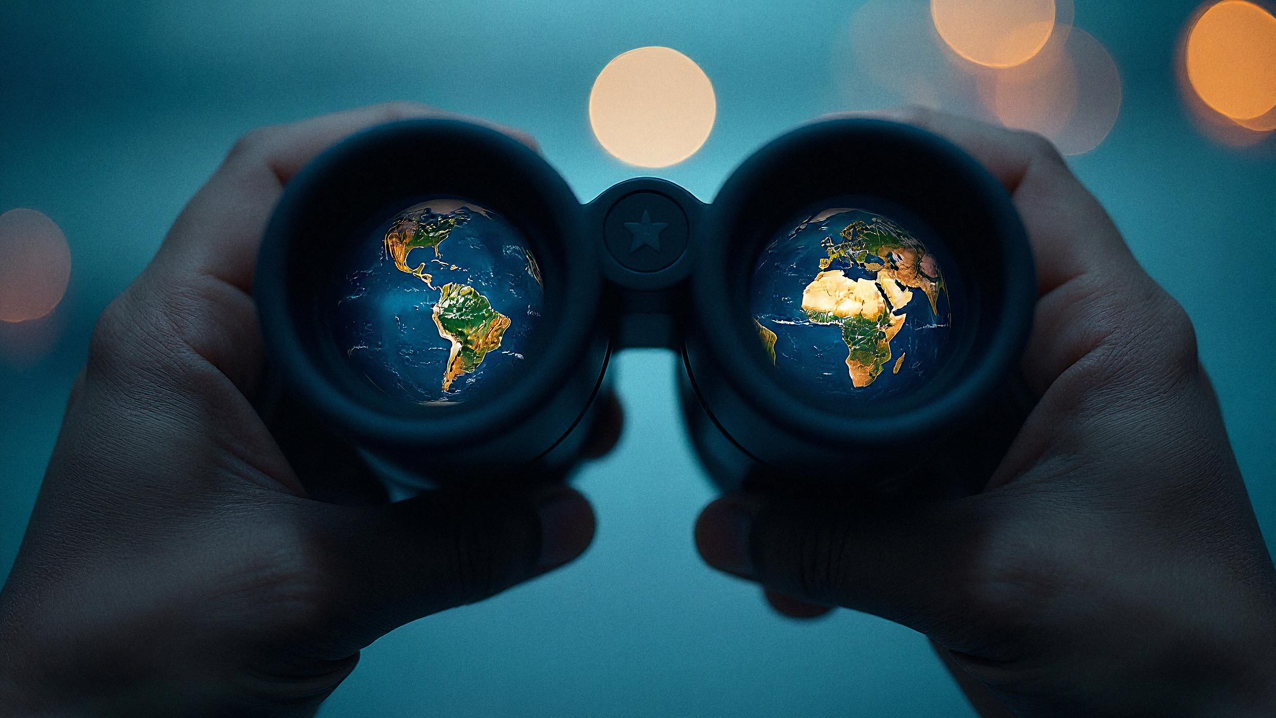 Hands holding binoculars with globes reflected in the lenses