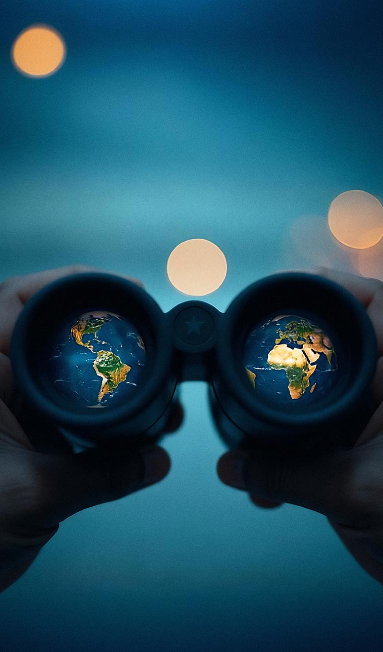 Hands holding binoculars with globes reflected in the lenses